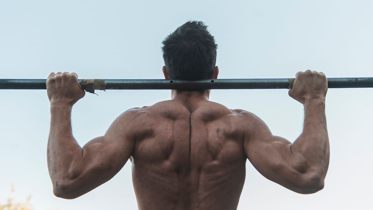 A person lifting a barbell outdoors, emphasizing back and shoulder muscle