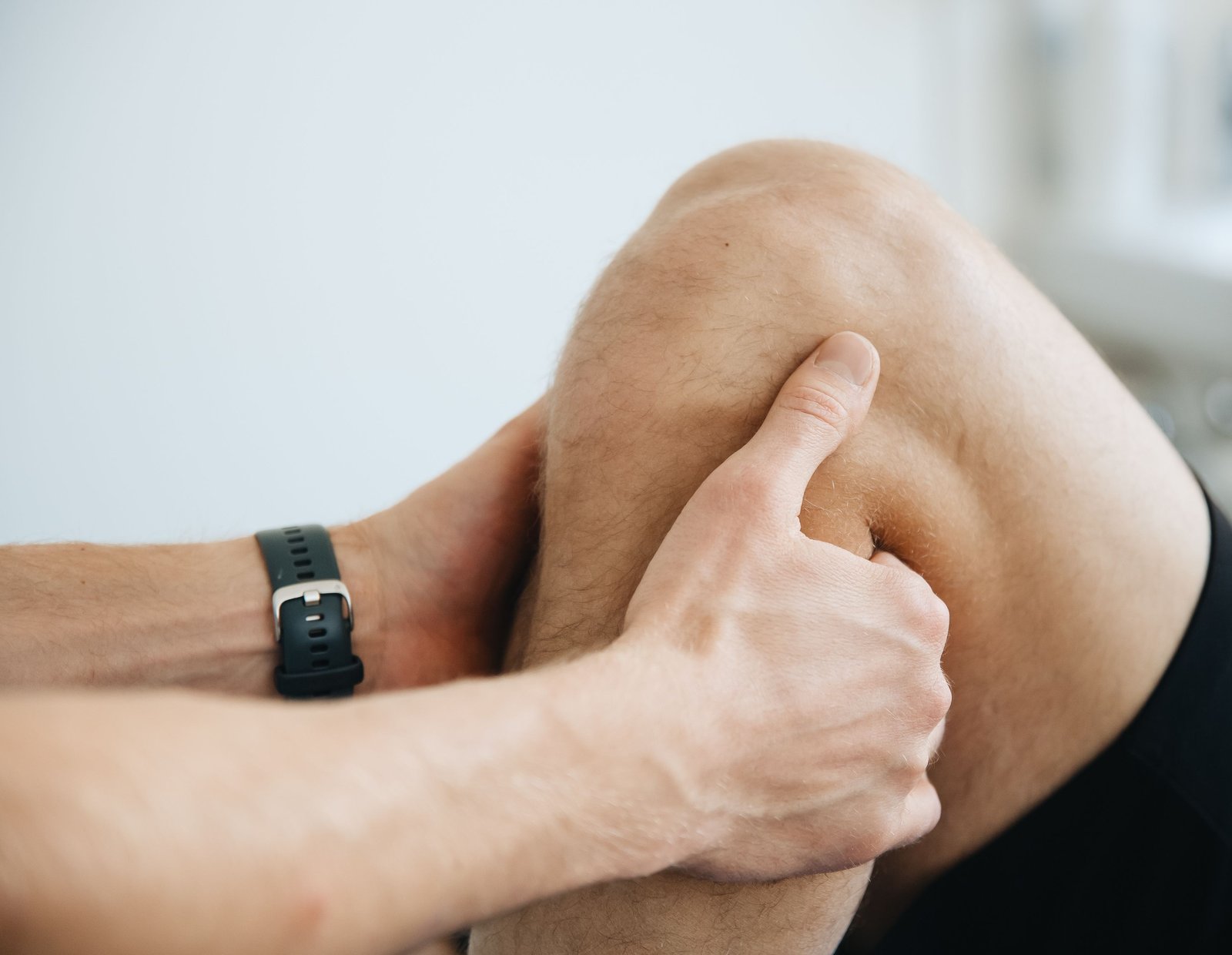 Close-up of a therapist's hands pressing on a person's bare knee during a physical-therapy session