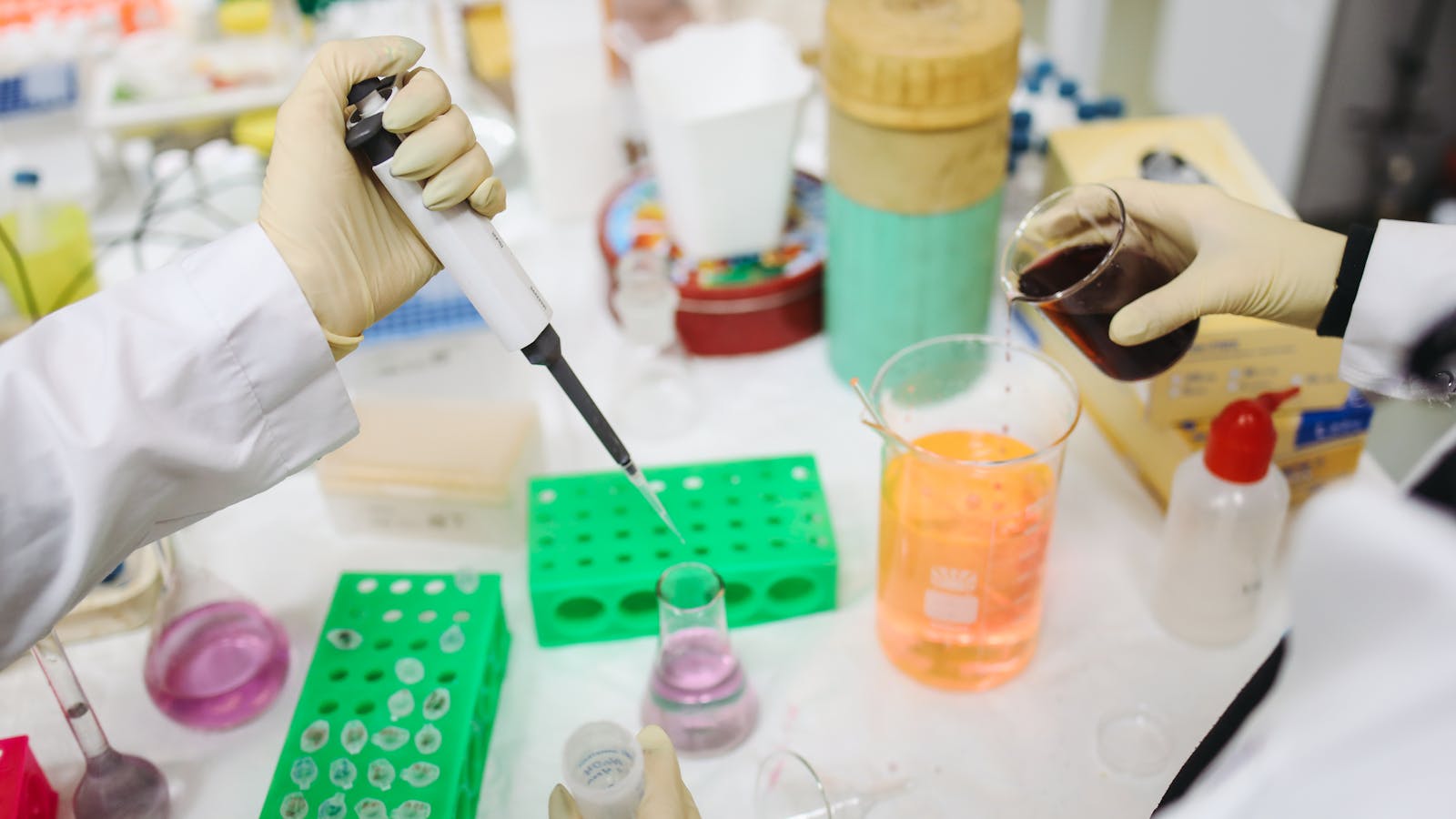 Gloved scientists pipetting and pouring colored solutions in a research laboratory