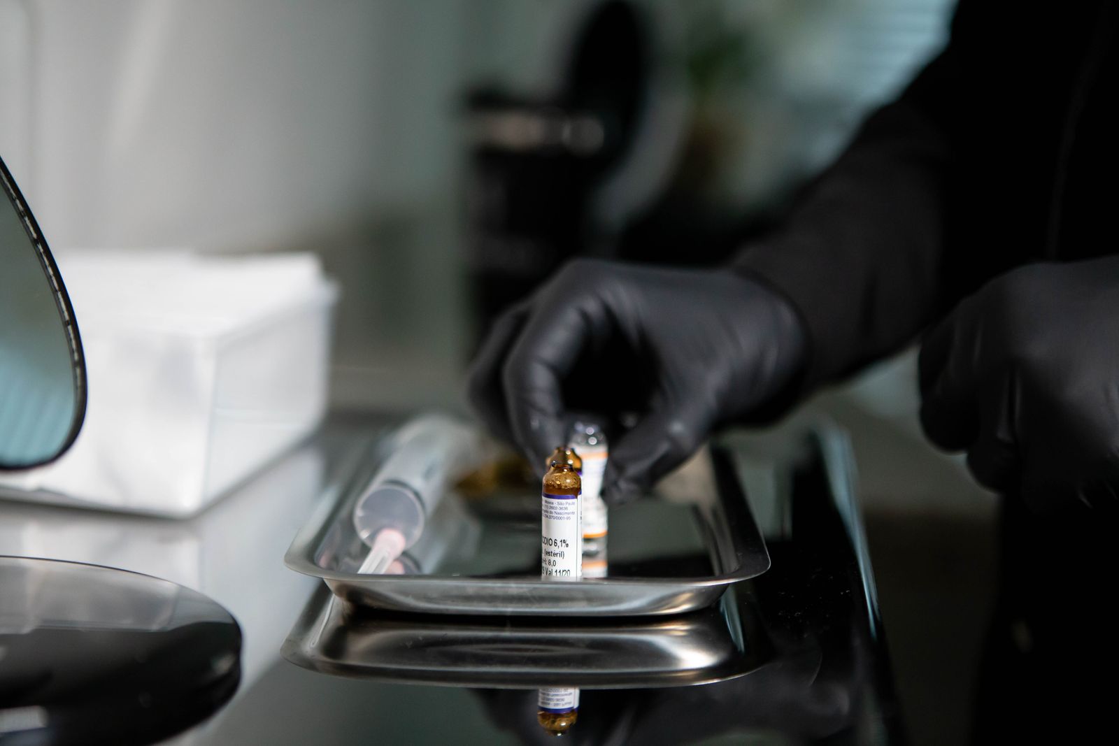 Gloved hands arranging small amber glass vials on a stainless tray beside a syringe, evoking research-vial handling of an unapproved injectable peptide
