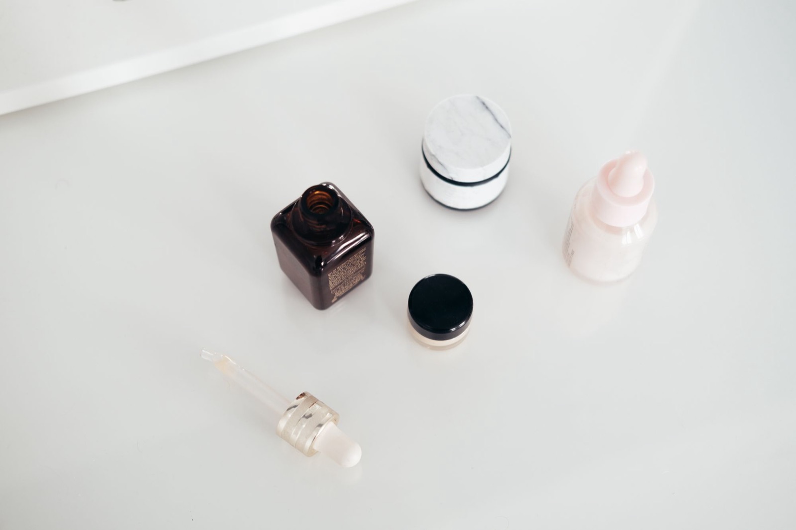 Flat lay of natural skincare products on white, including a glass serum dropper bottle and small jars, the topical cosmetic serums GHK-Cu is used in