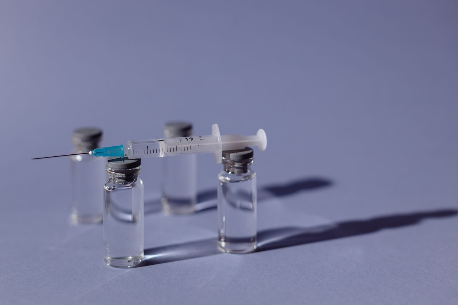 A syringe resting on top of small glass medication vials against a purple background