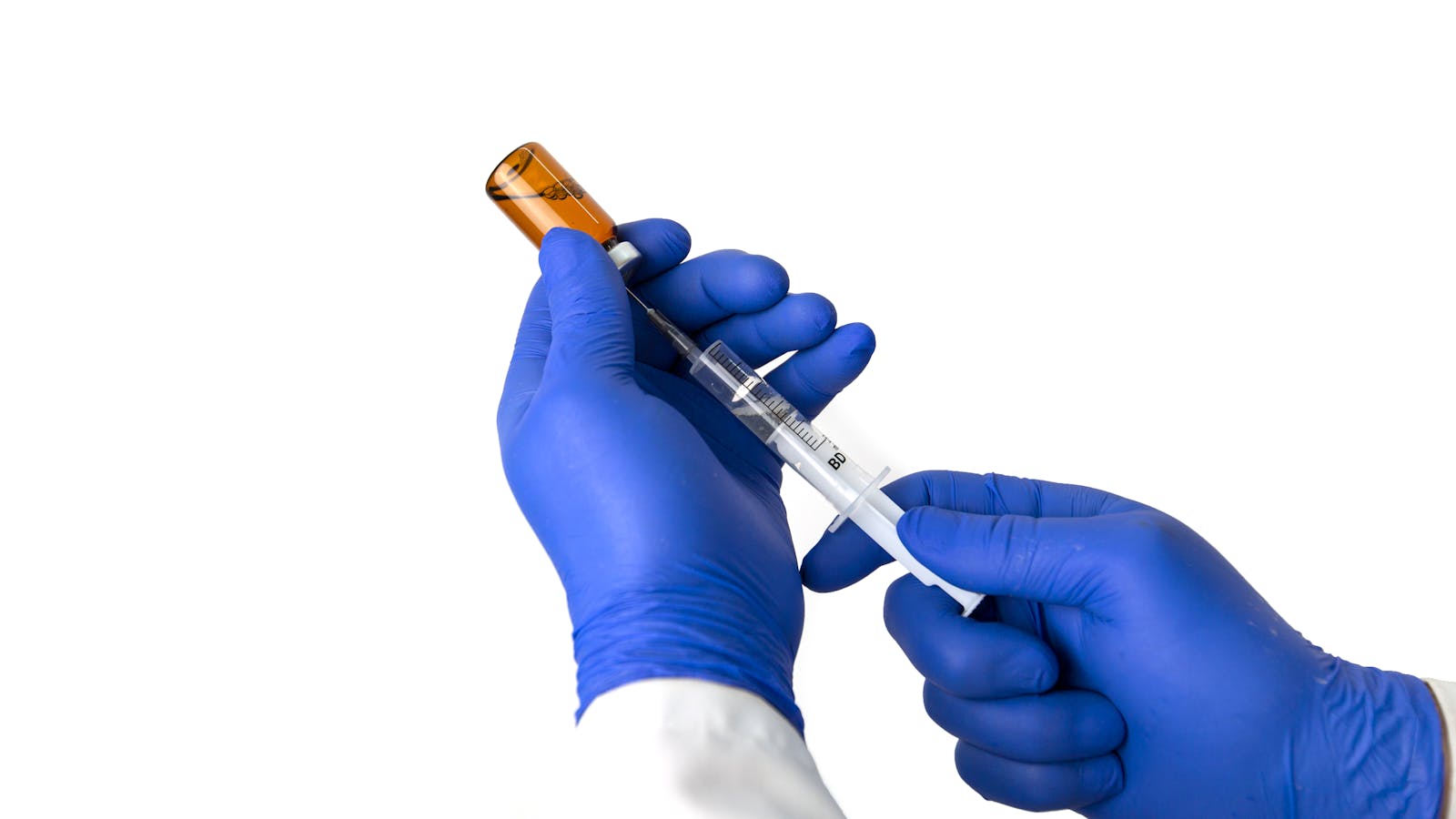 Gloved hands drawing medication into a syringe from a vial