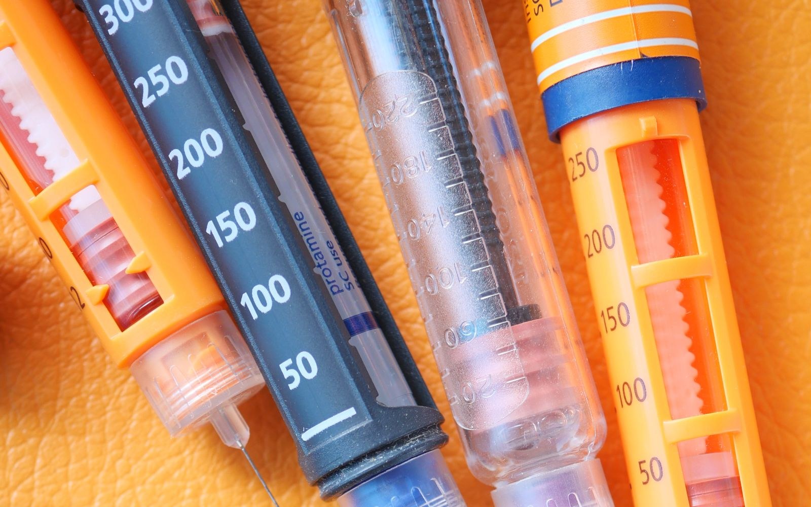 Close-up of several injection pens with dose-window markings lying on an orange surface, viewed from above