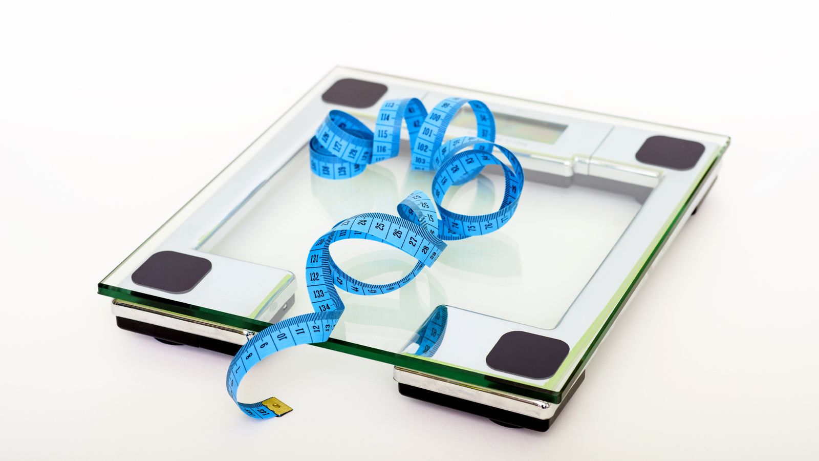 A clear glass bathroom scale with a blue tape measure resting on top, viewed from above