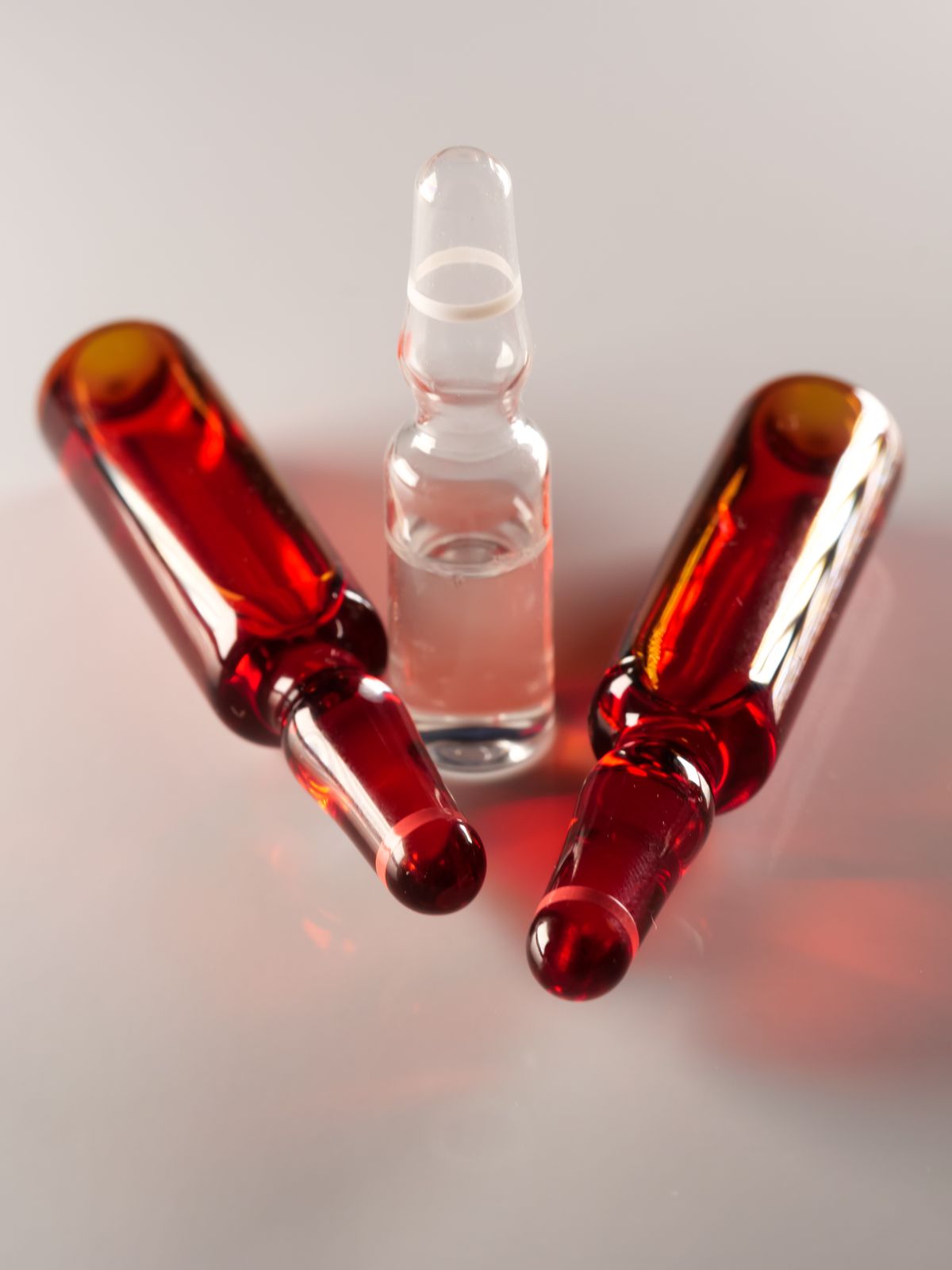 Three glass medicine ampoules, one clear and two amber, arranged on a pale surface