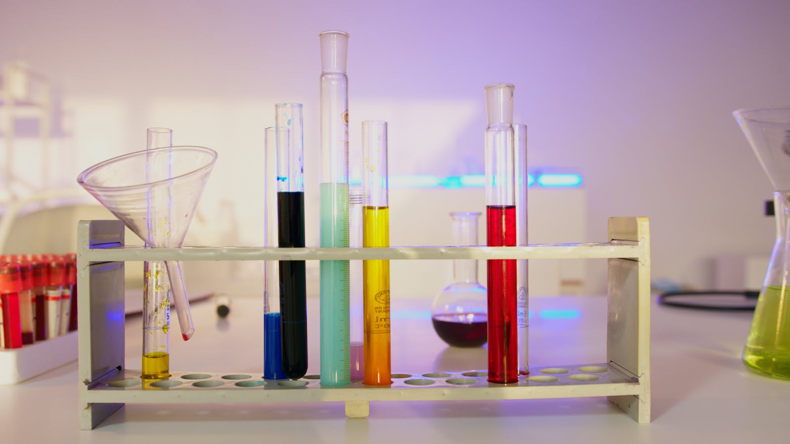 Laboratory test-tube rack holding clear glass tubes filled with assorted colored liquids
