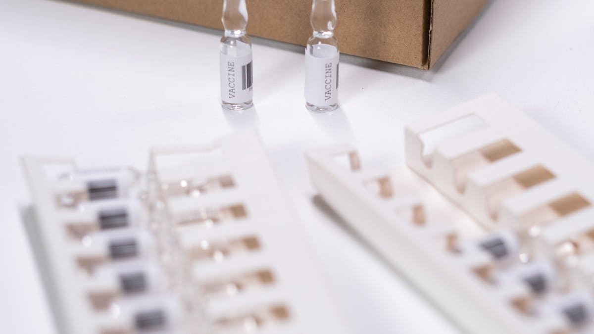 Small clear pharmaceutical vials arranged next to a cardboard packaging box