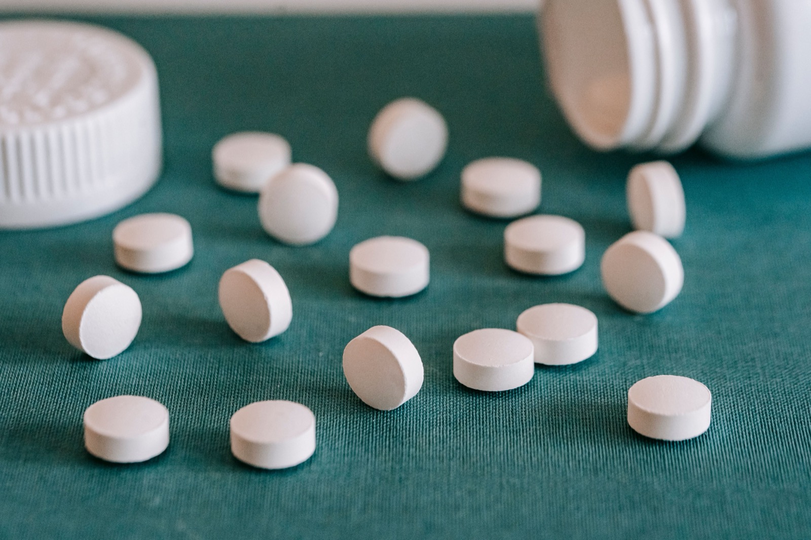 Round white tablets spilled from a container onto a plain surface, evoking that MK-677 is an oral pill you swallow rather than an injectable peptide