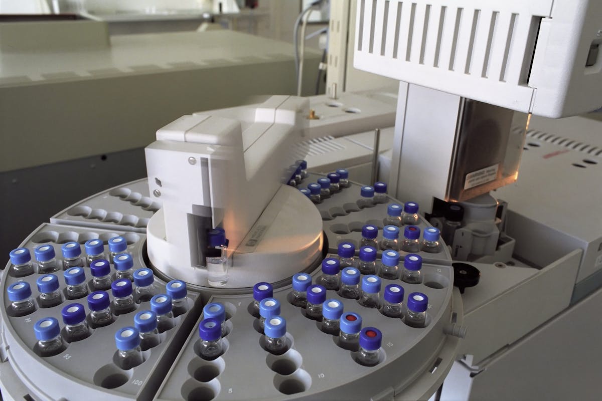 Rows of clear glass vials with blue crimp caps loaded into a chromatograph autosampler rack