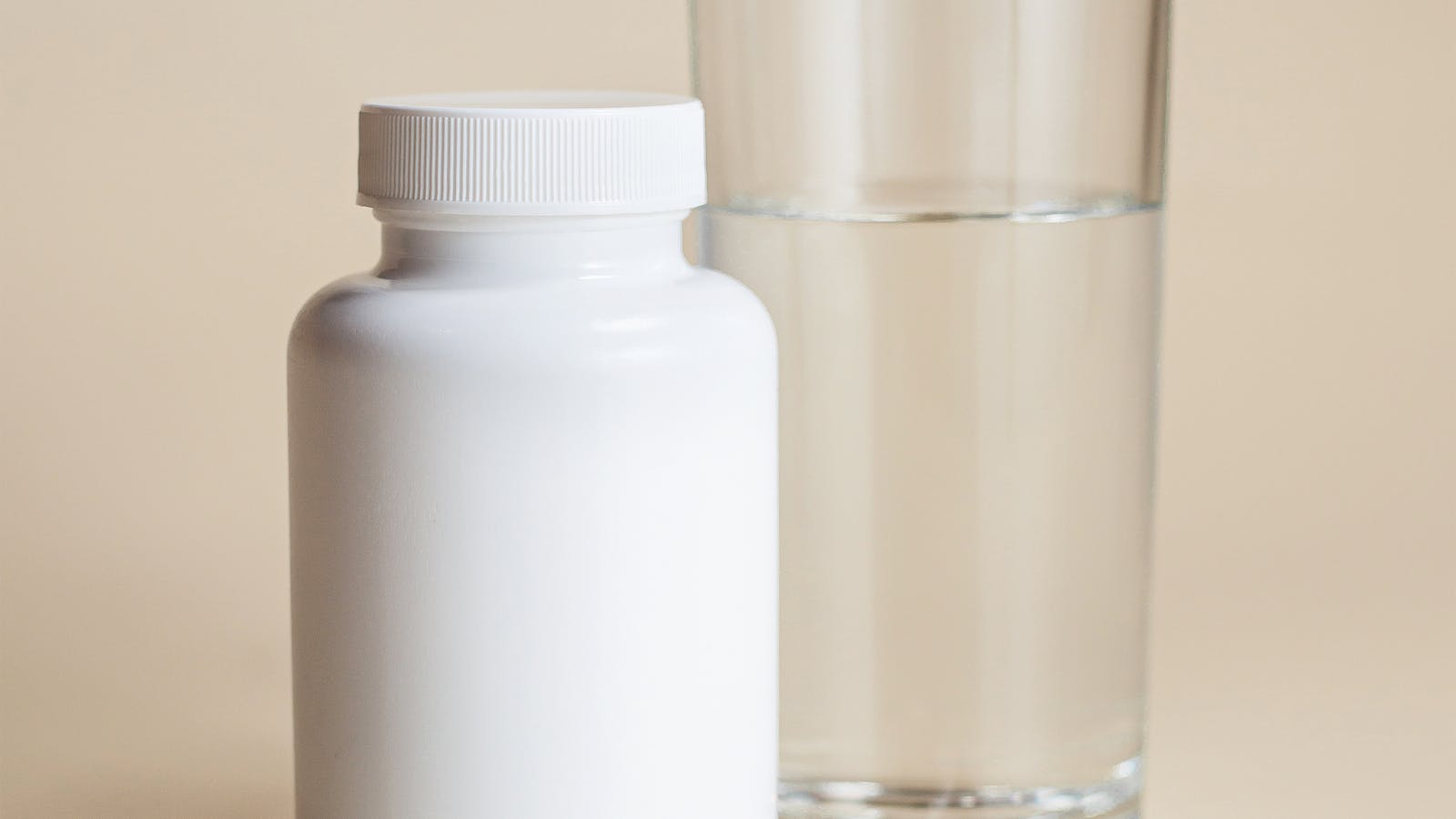 White supplement bottle next to a glass of water