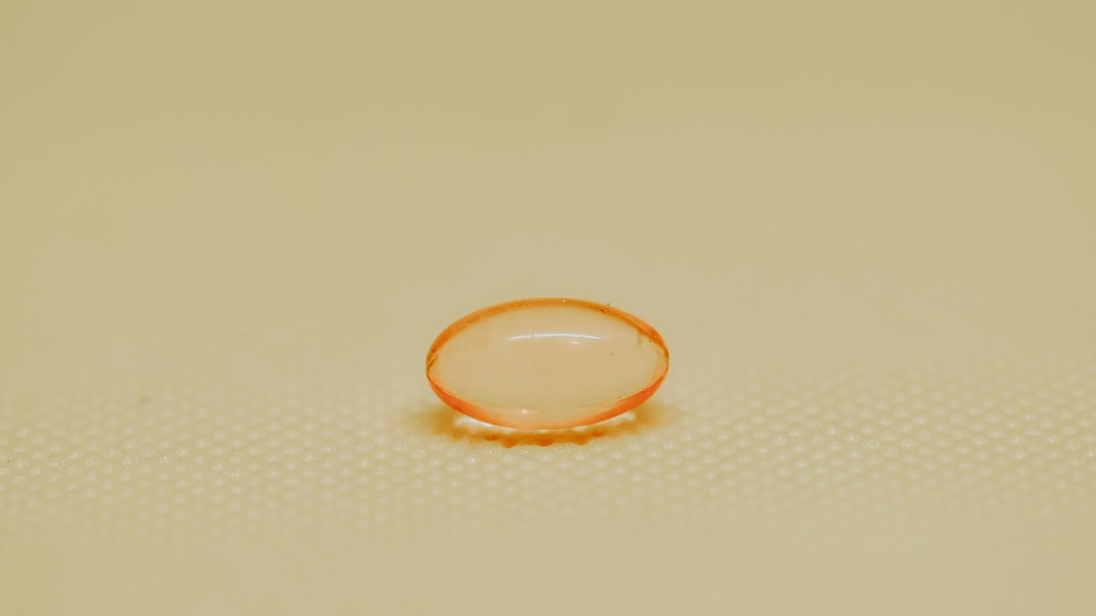 Extreme close-up of a single orange medicine capsule on a textured surface