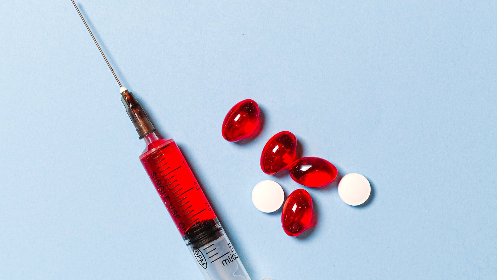 Syringe alongside a scatter of pills on a blue background