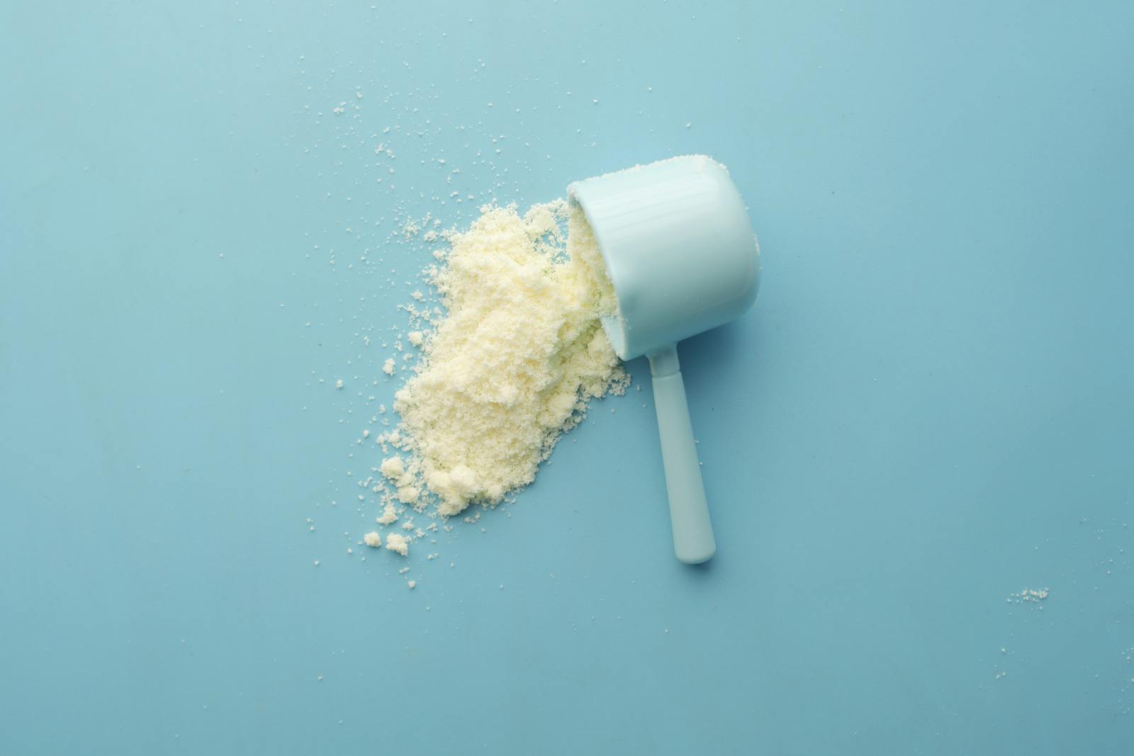Top-down still life of white powder spilling from a metal scoop against a saturated blue background