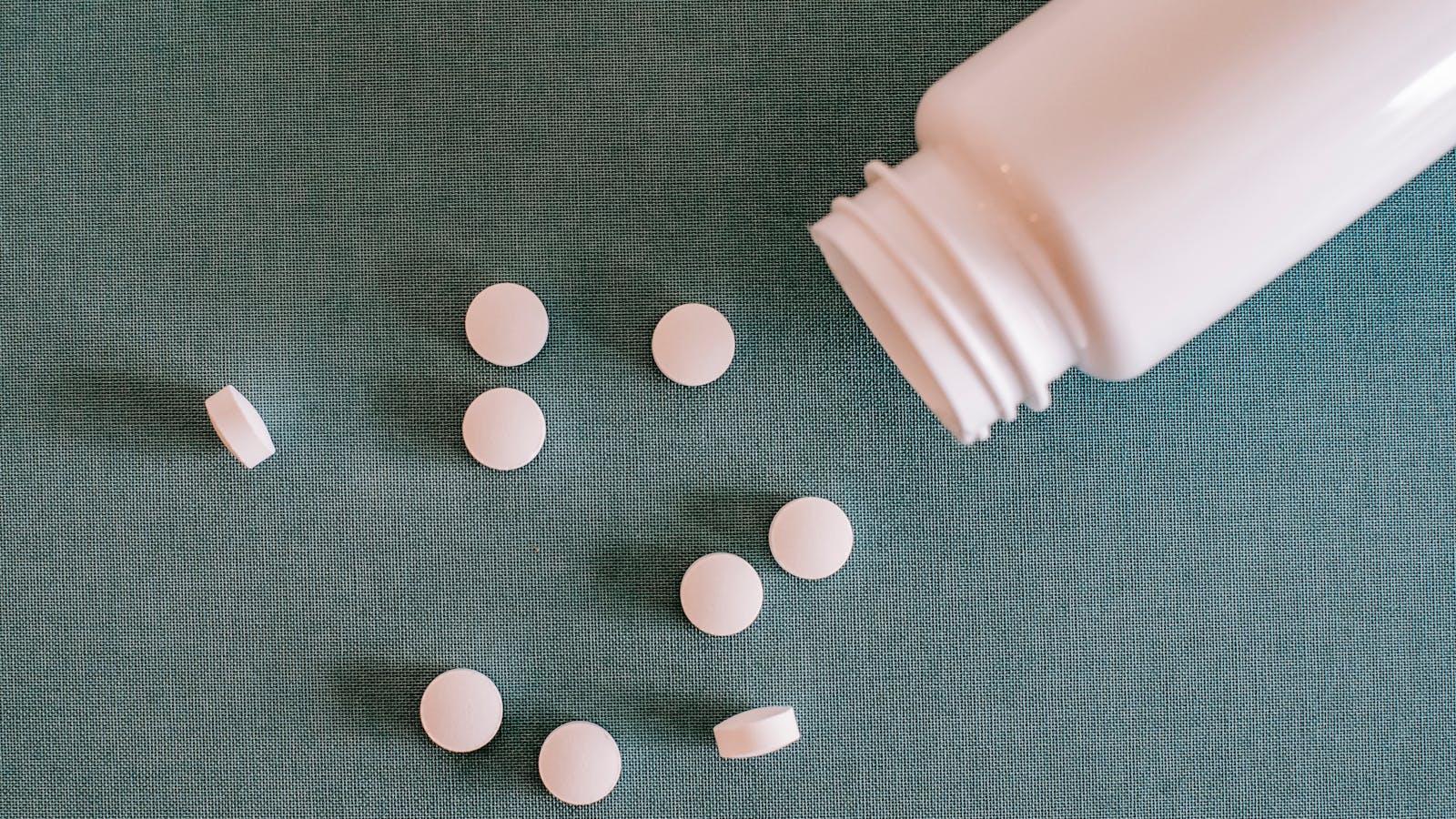 White pharmaceutical pills spilling from a plastic bottle