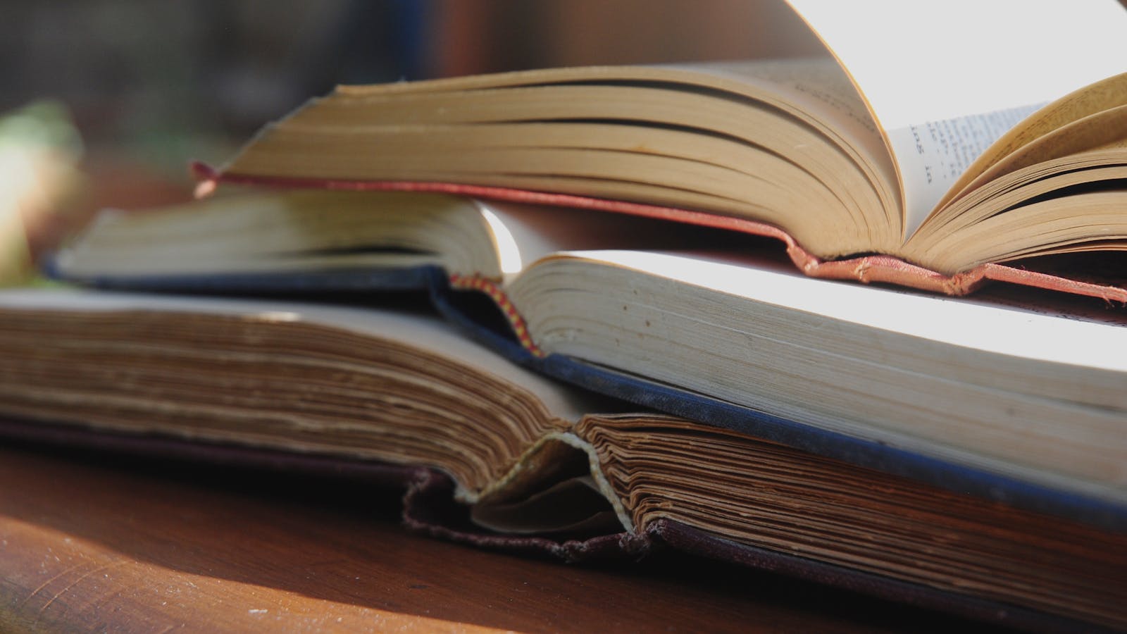 Stack of opened books on a sunlit wooden table