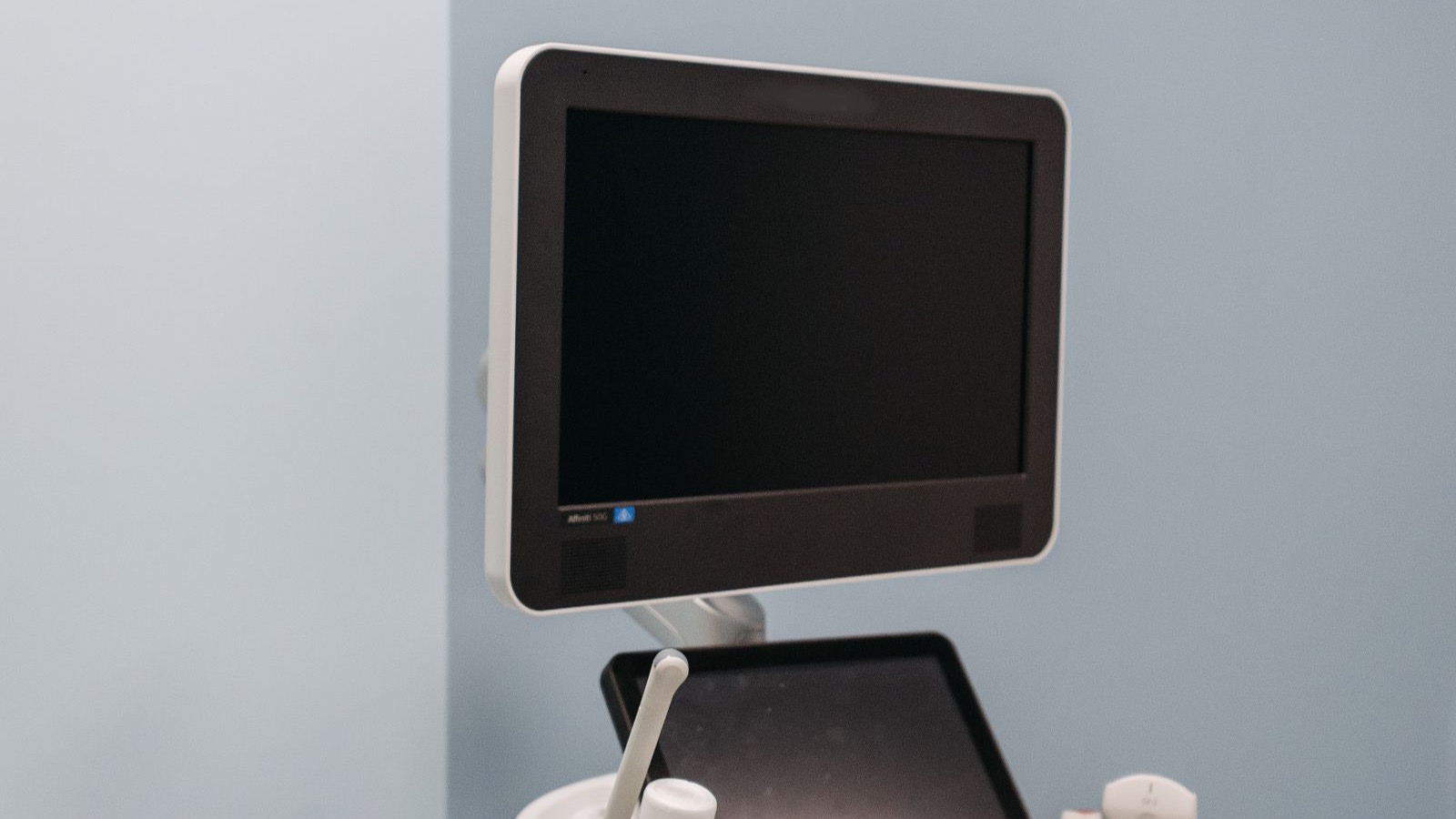 A digital medical ultrasound machine with a monitor and control panel standing in a clinical room