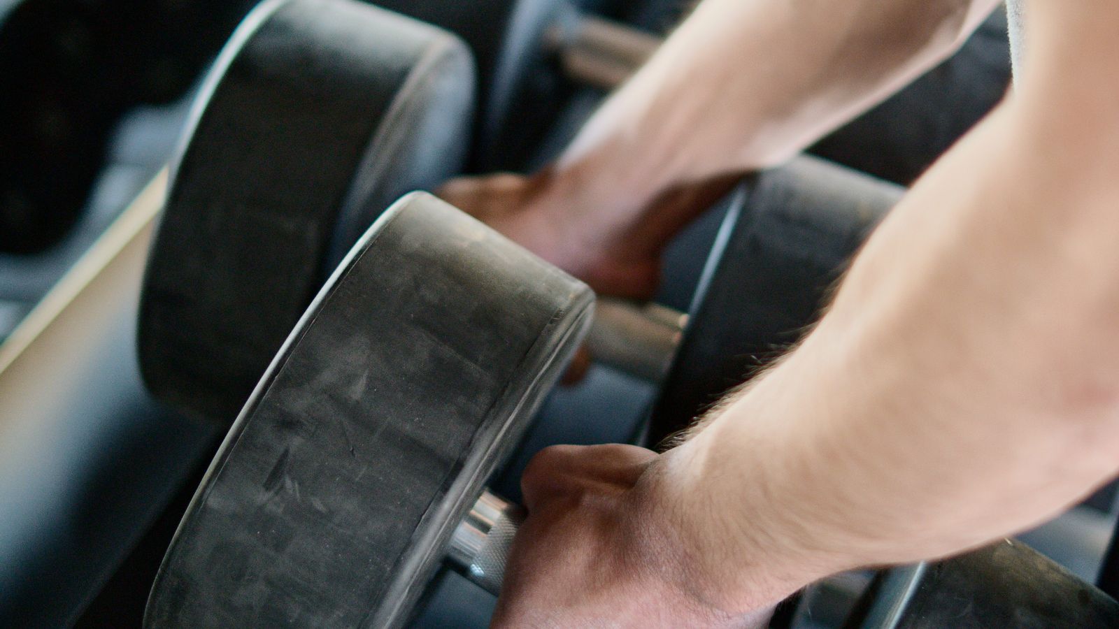 A person's hands lifting a pair of heavy black dumbbells off a gym rack, viewed close up, evoking resistance training to protect muscle during weight loss