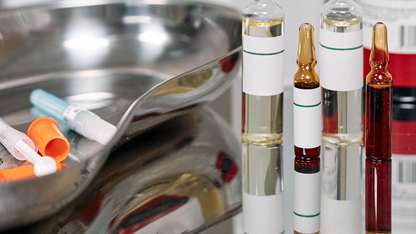 Four sealed glass ampoules standing side by side next to a steel tray of syringes