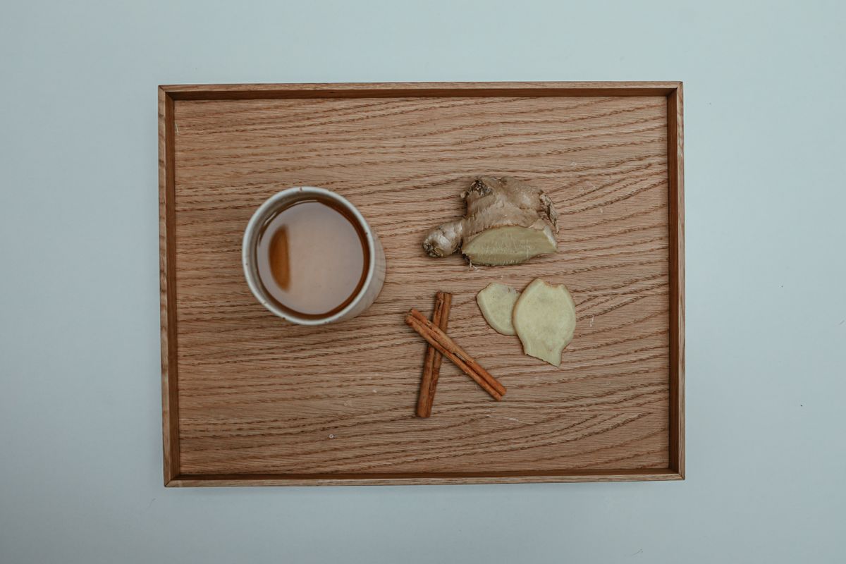 Overhead view of a cup of herbal tea with fresh ginger and cinnamon on a wooden tray