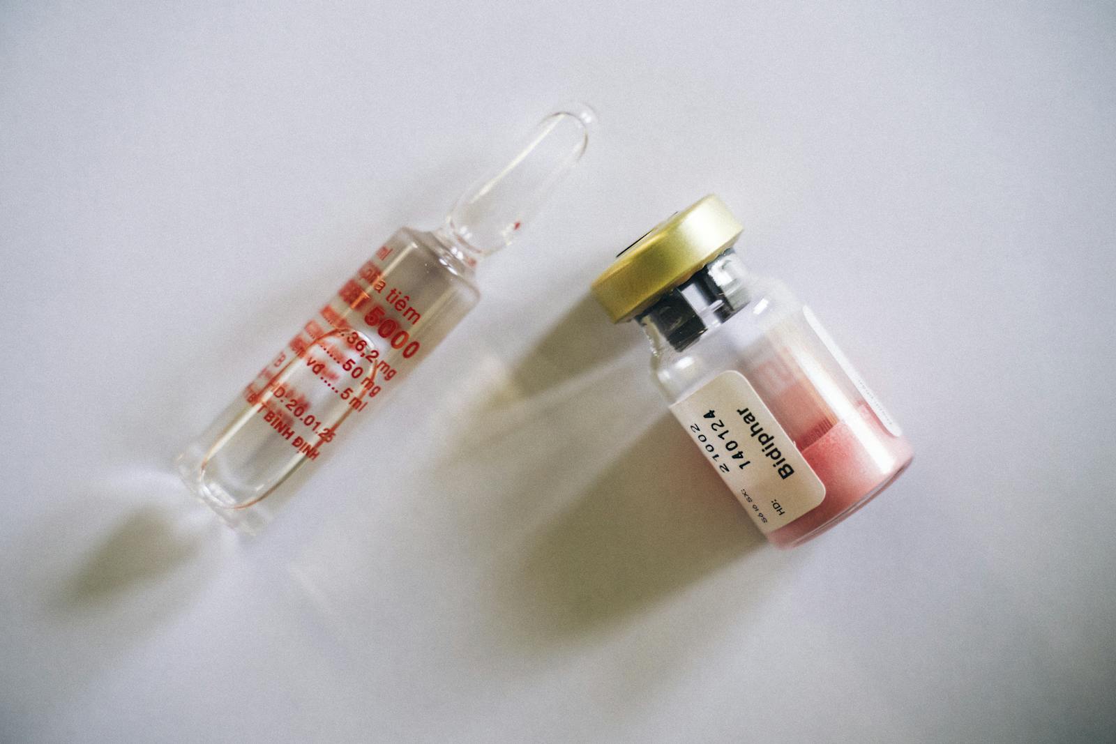 Top-down view of a single injection vial and ampoule on a clean white surface
