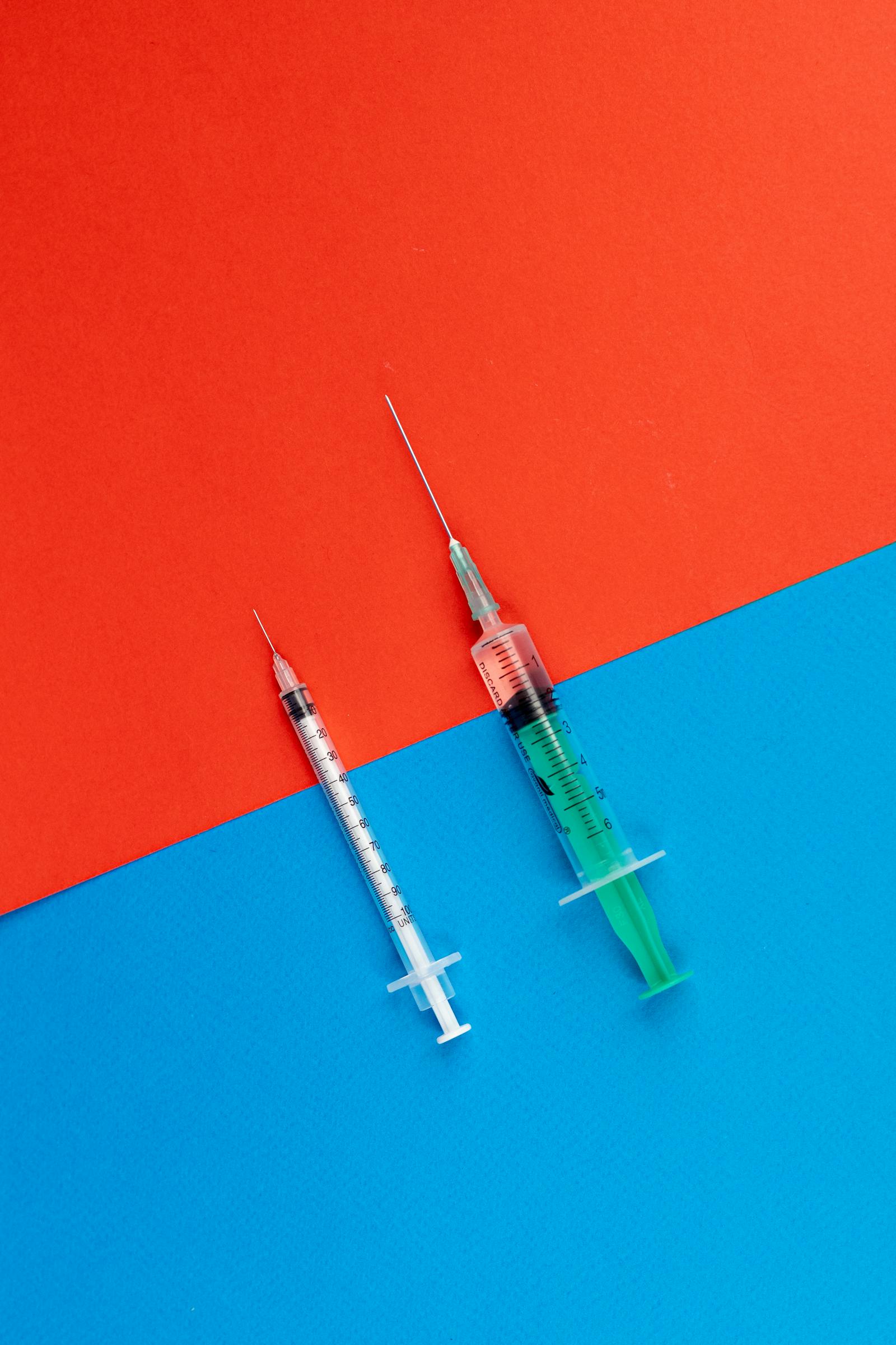 Two medical syringes laid side by side across a red and blue background
