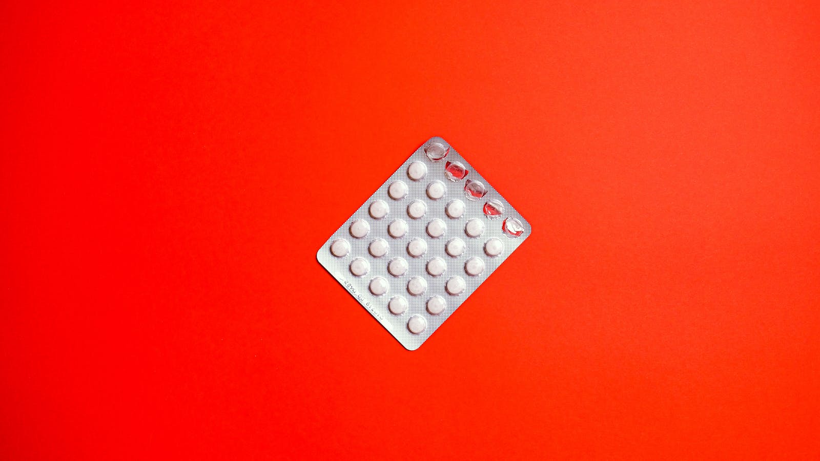 Silver blister pack of white pills against a red background