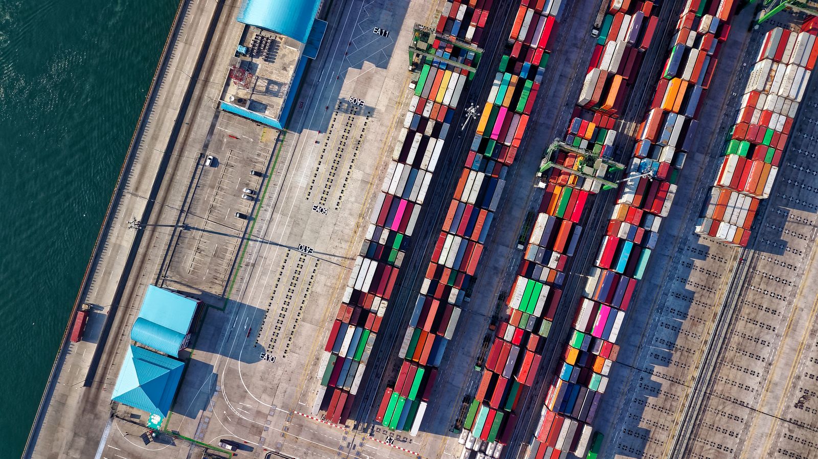 Aerial view of a shipping-container yard, rows of stacked intermodal cargo containers, evoking the global supply chain for active pharmaceutical ingredients