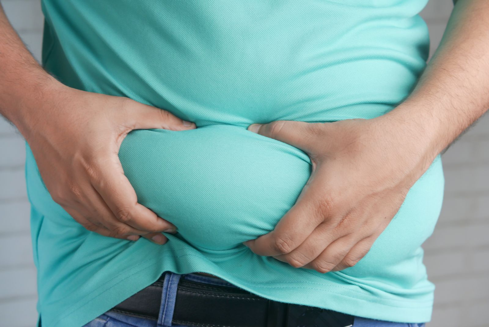 Close-up of a person's hands holding the excess fat around their midsection, evoking the deep abdominal (visceral) belly fat that tesamorelin is used to target