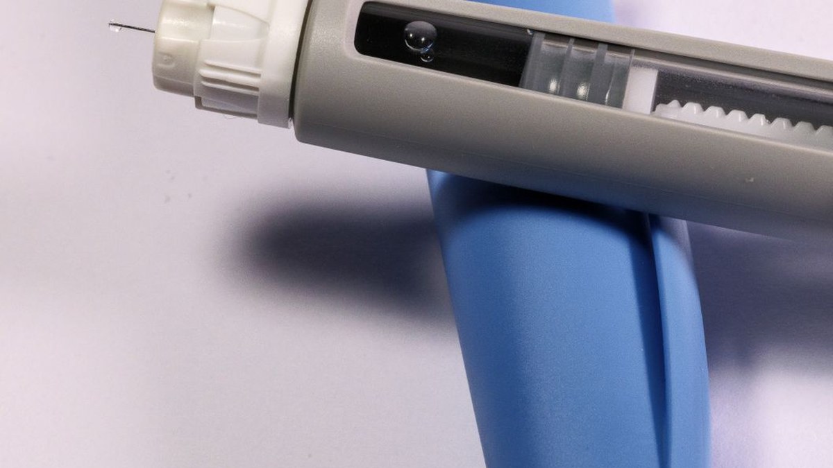 Close-up of an injectable medication pen showing the needle tip, dose window, and cap on a plain background