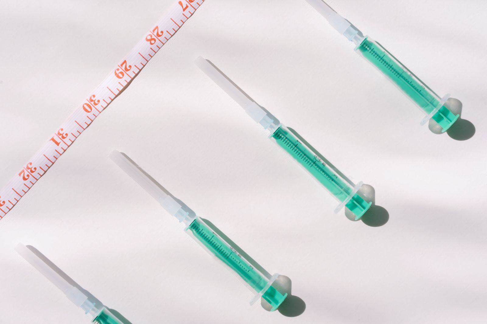 Overhead view of two filled injection syringes beside a yellow measuring tape on a white surface, evoking injectable weight-loss medication