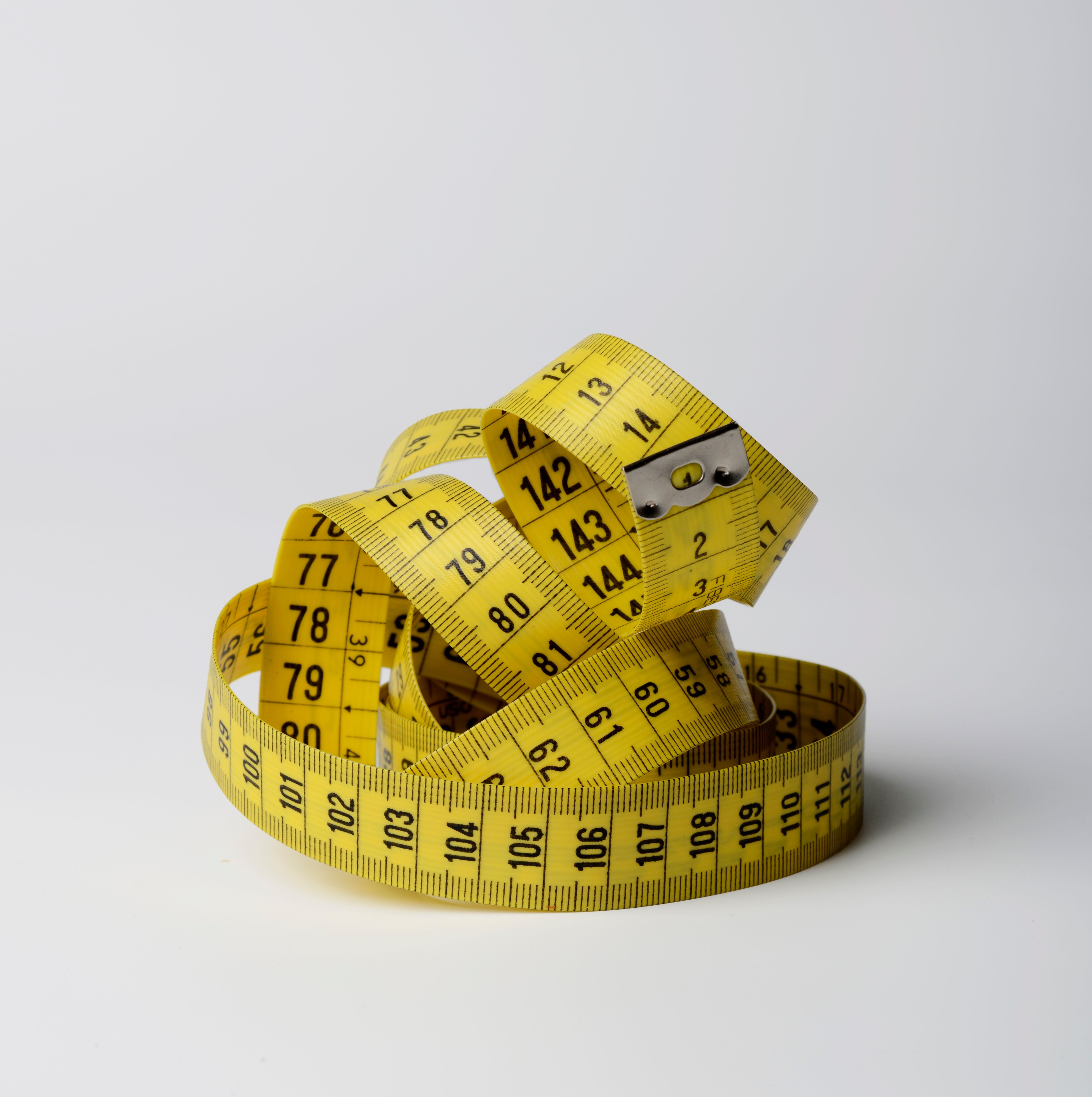 A bright yellow cloth measuring tape coiled in loops against a white background