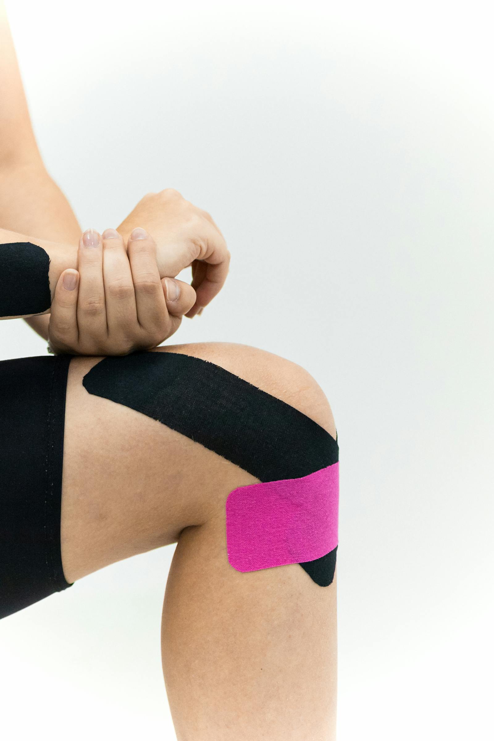 Close-up of an athlete's knee with black and pink kinesiology tape applied for joint support, against a clean white background